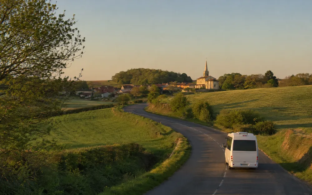 Un minibus Easy Mobility parcourt une route de campagne au coucher du soleil, vers un village au clocher